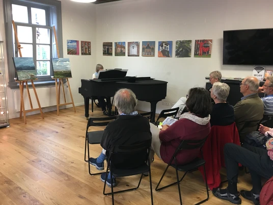 Musik zur Marktzeit Klavierkonzert in der Gaststube im Rathaus in Pewsum. Einige Besucher sitzen und lauschen den Klavierklängen von Annette Liss.