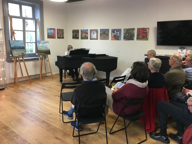 Musik zur Marktzeit Klavierkonzert in der Gaststube im Rathaus in Pewsum. Einige Besucher sitzen und lauschen den Klavierklängen von Annette Liss.