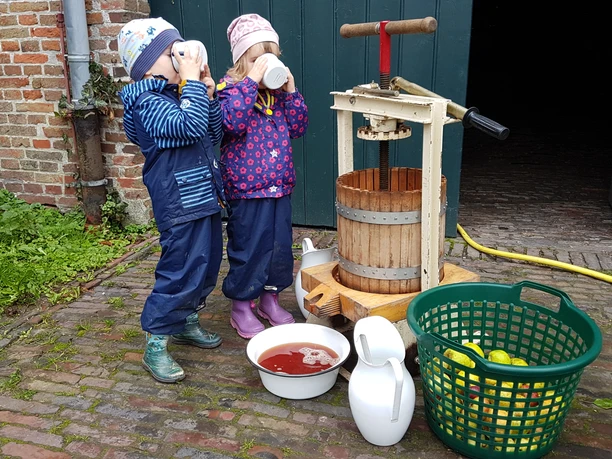 Apfelfest Zwei Kinder trinken frischen Apfelsaft neben einer alten Saftpresse beim Apfelfest in Campen.