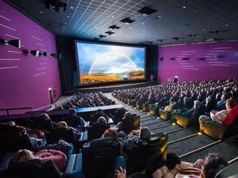 GRENZGANG im Cinedom Menschen in einem großen Kinosaal beobachten gespannt eine eindrucksvolle Projektion auf großer Leinwand.People in a large movie theater watch an impressive projection on a big screen.