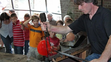 Glasmacher.jpg Ein Glasmacher fertigt vor einer staunenden Kindergruppe eine leuchtend rote Glaskugel an.