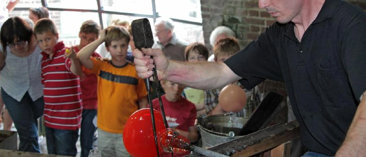 Glasmacher.jpg Ein Glasmacher fertigt vor einer staunenden Kindergruppe eine leuchtend rote Glaskugel an.