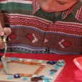 Überraschungswerkstatt 2.jpg Ein Kind verziert konzentriert eine Holzplatte mit bunten Glasstücken und hebt sie sorgsam an.