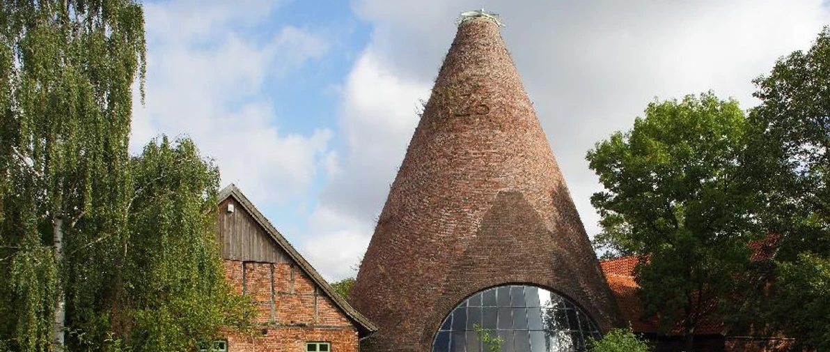 LWL Glashütte Gernheim.jpg Rundofen der LWL-Glashütte Gernheim mit markantem Schornstein, umgeben von üppigem Grün und Bäumen.