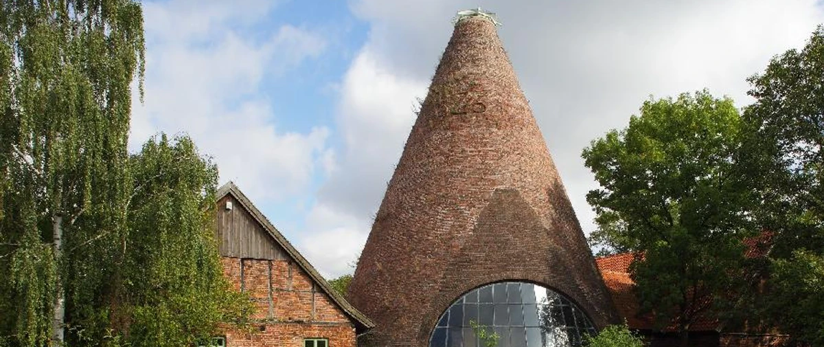 LWL Glashütte Gernheim.jpg Rundofen der LWL-Glashütte Gernheim mit markantem Schornstein, umgeben von üppigem Grün und Bäumen.