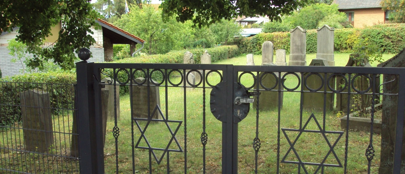 Jüdischer Friedhof Salzgitter-Bad (8)_HD.JPG Schwarzes Eisentor mit Davidsternen vor einem jüdischen Friedhof mit alten Grabsteinen.
