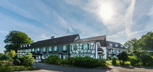 Außenansicht von Lohmanns Romantik Hotel Gravenberg in Langenfeld Fachwerkgebäude von Lohmanns Romantik Hotel Gravenberg in Langenfeld mit grünen Akzenten unter blauem Himmel.