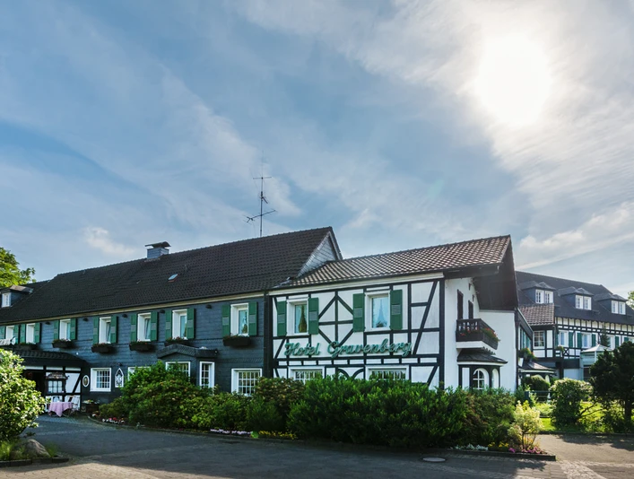 Außenansicht von Lohmanns Romantik Hotel Gravenberg in Langenfeld Fachwerkgebäude von Lohmanns Romantik Hotel Gravenberg in Langenfeld mit grünen Akzenten unter blauem Himmel.