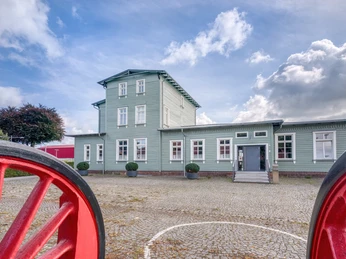 Bahnhof Rahden Historischer Bahnhof Rahden, grünes Gebäude, Dreigeschossturm, Kopfsteinpflaster, blühende Sträucher.