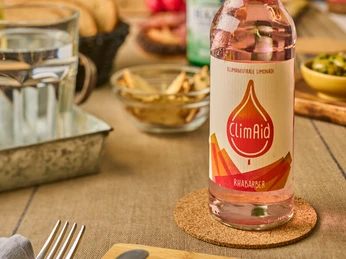 ClimAid Limonade Rhabarber ClimAid Limonade in Rhabarber-Geschmack steht auf einem Tisch neben Schalen und einem Glas Wasser.