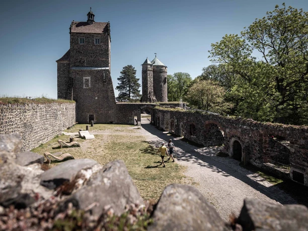 The fourth courtyard at Stolpen Castle Historic Stolpen Castle with two stone towers, surrounded by green trees; two people strolling in the courtyard in sunny weather.