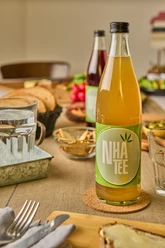 Königs NHA Hanftee Eine goldene Flasche Hanftee mit grünem Etikett steht auf einem gedeckten Tisch mit Snacks.