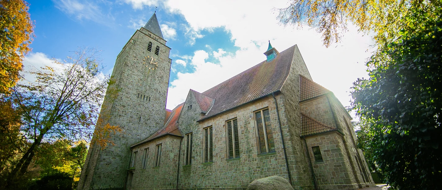 Kath.Kirche-St.Ludgerus_Schapen©MedienAtelierEmsland.jpg Historische Kirche aus hellem Naturstein mit Glockenturm und rotem Ziegeldach unter blauem Himmel
