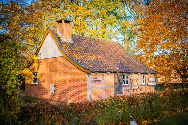 Alte-Schmiede-Laake_Varenrode©MedienAtelierEmsland.jpg Backsteinbau mit Ziegeldach und Schornstein, umgeben von herbstlichen Bäumen in warmem Licht