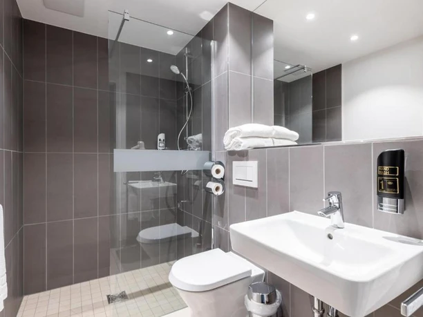 Hotelbadezimmer im Serways Hotel Hösel in Ratingen Modernes Hotelbadezimmer mit barrierefreier Dusche, sauberem Waschbecken und dezentem Beleuchtungskonzept.