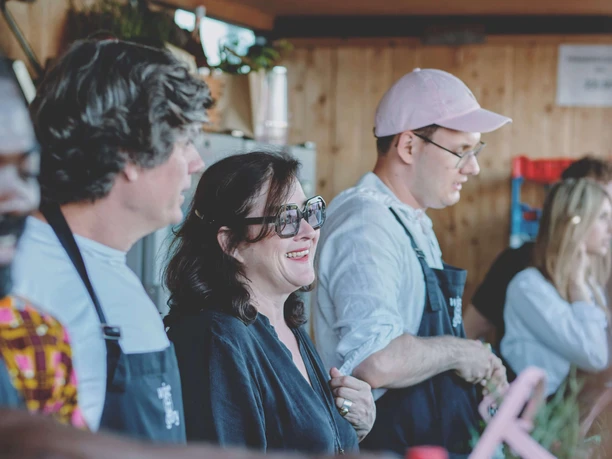 Weinfest am Rhein In einem gemütlichen Pavillon stehen mehrere Menschen hinter einer Theke und schenken Wein aus. Eine Frau mit Sonnenbrille lächelt fröhlich und unterhält sich mit einer Person, die nicht im Bild zu sehen ist. Blauer Himmel und Holzverkleidung vermitteln eine entspannte Stimmung.
