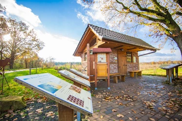 Bienenhaus_Venhaus©MedienAtelierEmsland.jpg Kleines Backsteinhaus mit Infotafeln zur Imkerei, umgeben von Wiese und herbstlichen Bäumen.