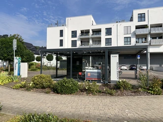 Ladeschrank Moderne Fahrradservicestation an einer hellen Wohnanlage mit überdachten Stellplätzen und Infotafel.