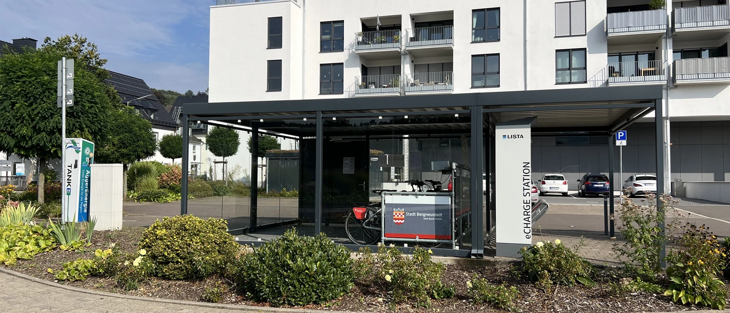 Ladeschrank Moderne Fahrradservicestation an einer hellen Wohnanlage mit überdachten Stellplätzen und Infotafel.