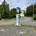 Ladesäule Parkplatz mit Ladestation für Elektrofahrzeuge, umgeben von Bäumen und einem Mehrfamilienhaus.
