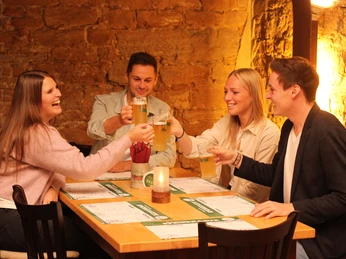 Vier junge Erwachsene stoßen fröhlich mit Biergläsern in einer rustikalen Brauerei an.