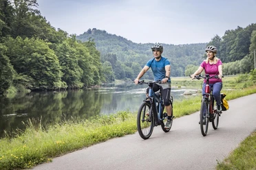 Radfahrer am Regental-Radweg Zwei Radfahrer fahren auf einem geteerten Abschnitt entlang des Regental-Radwegs. Im Hintergrund sieht man den Regen und die Burg Stockenfels.