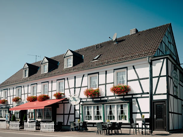 Außenansicht Ein traditionelles Fachwerkhaus mit bunten Blumen im Erdgeschossbereich unter strahlend blauem Himmel.