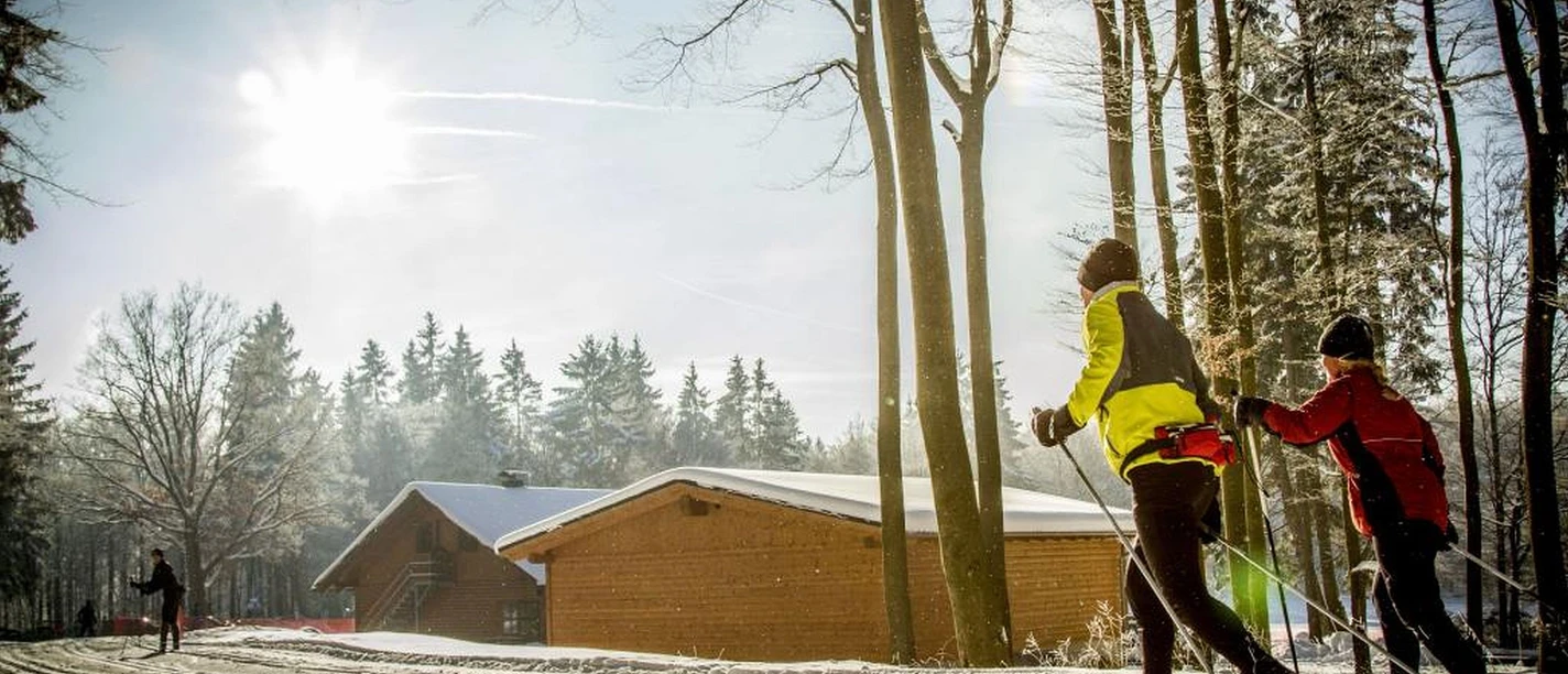Langläufer in der Loipe vor Holzhütten Langläufer in der Loipe vor Holzhütten
