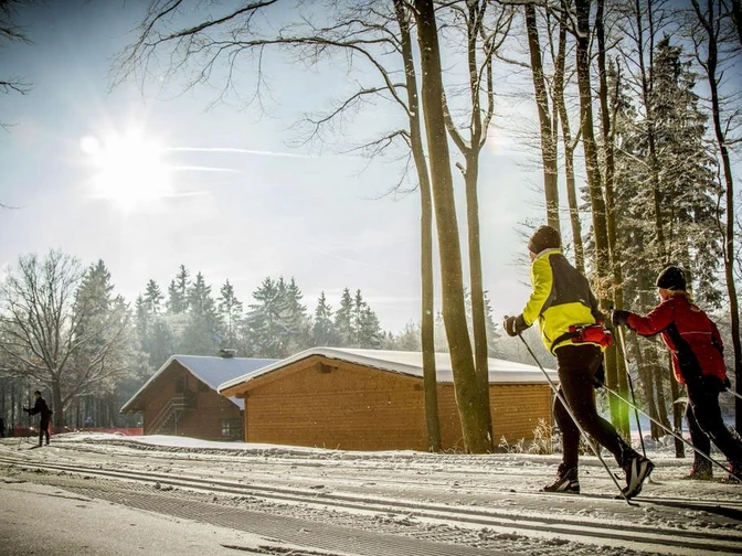 Langläufer in der Loipe vor Holzhütten Langläufer in der Loipe vor Holzhütten
