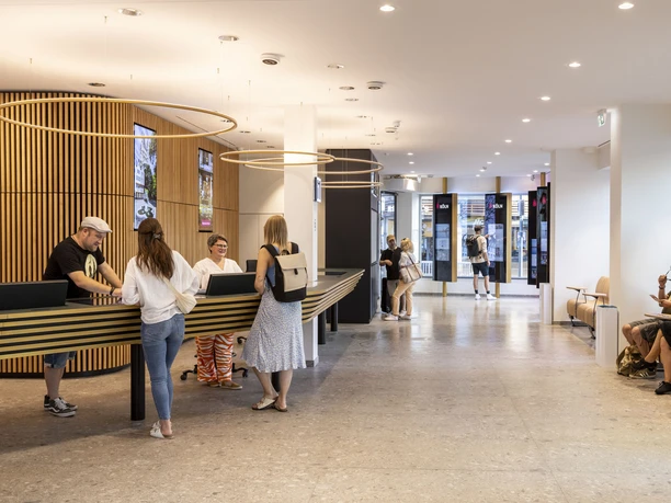 Tourist Information Köln Besucher im modernen Foyer der Tourist-Information Köln am Tresen bei der Beratung.