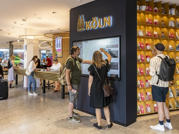 Tourist Information Köln Besucher nutzen interaktive Bildschirme in einer modernen Touristeninformation in Köln.