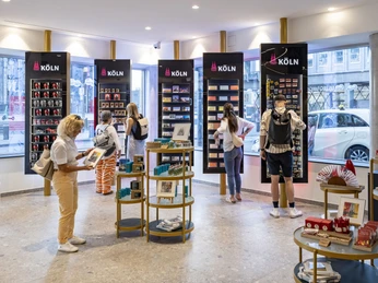 Tourist Information Köln Innenansicht der Kölner Touristeninformation mit Besuchern, die Souvenirs durchstöbern.Interior view of the Cologne tourist information office with visitors browsing through souvenirs.