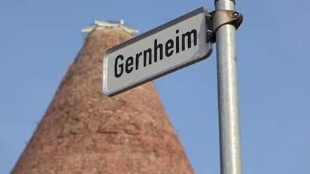 Gernheim.jpg Straßenschild mit Aufschrift "Gernheim" vor einem hohen, turmförmigen Backsteingebäude.