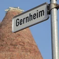 Gernheim.jpg Straßenschild mit Aufschrift "Gernheim" vor einem hohen, turmförmigen Backsteingebäude.