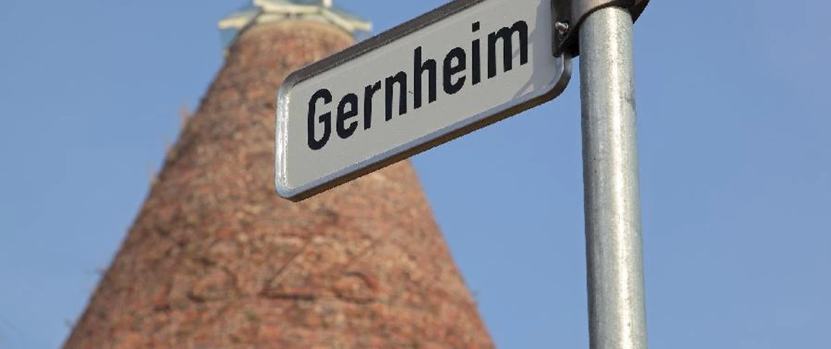 Gernheim.jpg Straßenschild mit Aufschrift "Gernheim" vor einem hohen, turmförmigen Backsteingebäude.