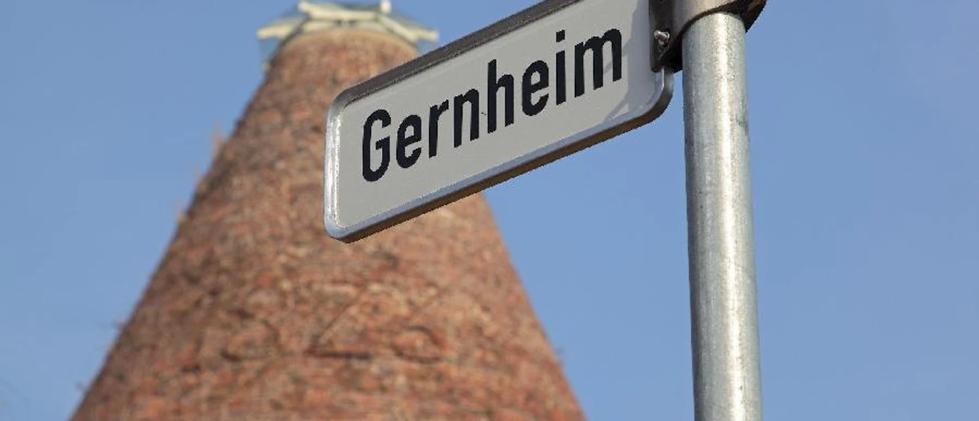 Gernheim.jpg Straßenschild mit Aufschrift "Gernheim" vor einem hohen, turmförmigen Backsteingebäude.