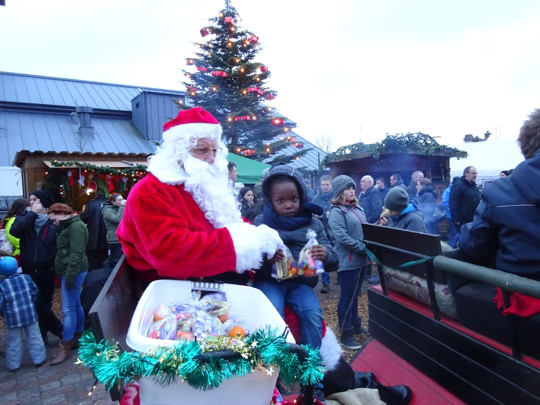 Weihnachtsmann mit Kutsche Weihnachtsmann in rotem Mantel auf Kutsche verteilt Süßigkeiten an Kinder auf festlichem Markt.Santa Claus in a red coat on a carriage hands out sweets to children at a festive market.Julemanden i en rød frakke på en vogn deler slik ud til børn på et festligt marked.De Kerstman in een rode jas op een koets deelt snoep uit aan kinderen op een feestelijke markt.