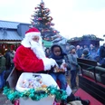 Weihnachtsmann mit Kutsche Weihnachtsmann in rotem Mantel auf Kutsche verteilt Süßigkeiten an Kinder auf festlichem Markt.Santa Claus in a red coat on a carriage hands out sweets to children at a festive market.Julemanden i en rød frakke på en vogn deler slik ud til børn på et festligt marked.De Kerstman in een rode jas op een koets deelt snoep uit aan kinderen op een feestelijke markt.