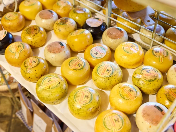 Hofladen Hielscher Hof Kleine runde Käselaibe in verschiedenen Farben und Geschmäckern auf einem Marktstand ausgestellt.