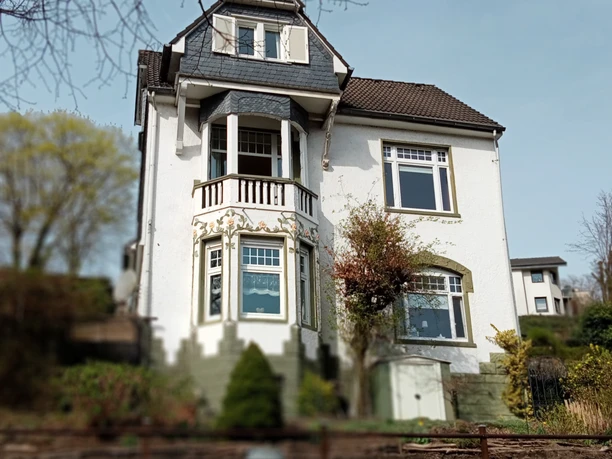 Fewo Villa Neviges in Velbert-Neviges Weiße, zweistöckige Villa mit dunklem Dach, großen Fenstern und dekorativen Balkonen umgeben von Grün.