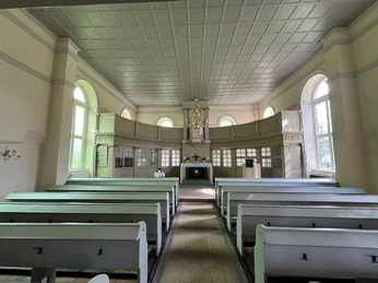 Heller Innenraum der Kirche Oiste mit Holzbänken, Altar, großen Fenstern und einem Kronleuchter.