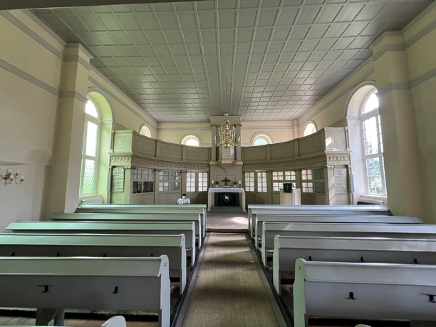 Heller Innenraum der Kirche Oiste mit Holzbänken, Altar, großen Fenstern und einem Kronleuchter.
