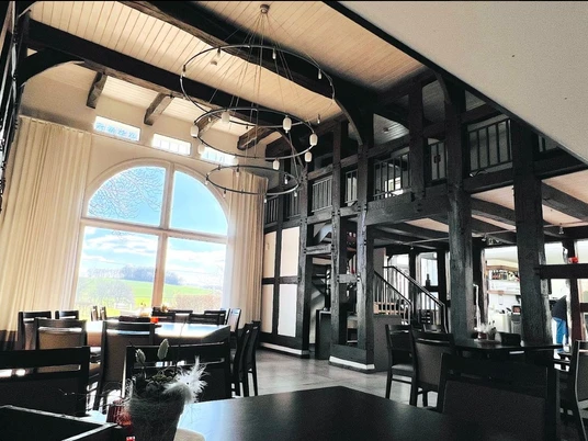 Ziegler.jpg Restaurant mit hohen Decken und rustikalen Holzbalken, großen Fenstern mit Aussicht auf Felder.