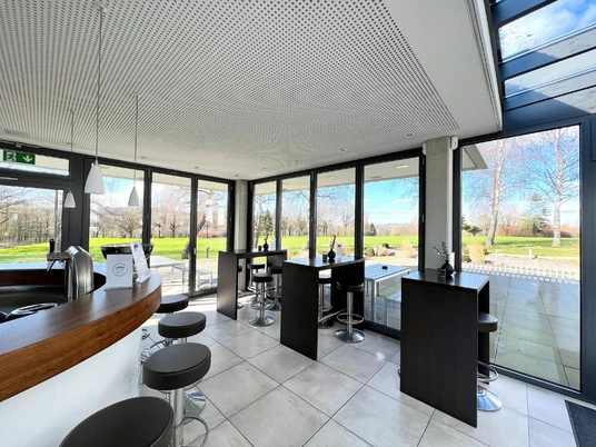 Ziegler_1.jpg Großzügiges Café mit modernen, bodentiefen Fenstern, hellen Fliesen und eleganten Sitzmöbeln.