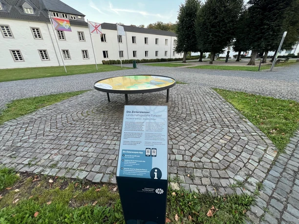 3D-Landschaftsmodell Klosterlandschaft Altenberg In der Mitte eines gepflasterten Platzes steht eine Informationstafel vor einem großen, runden Reliefmodell.