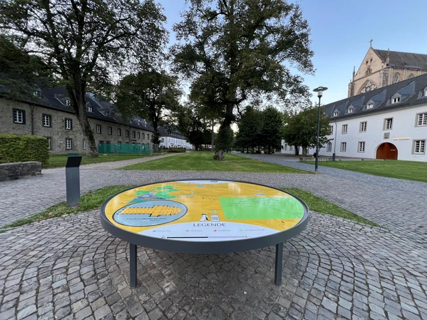 3D-Landschaftsmodell Klosterlandschaft Altenberg Ein informativer, runder Lageplan in einem gepflasterten Innenhof, umgeben von historischen Gebäuden.
