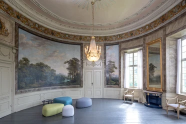 Eleganter, runder Saal mit historischen Wandmalereien, imposantem Kronleuchter und modernen Sitzhockern.