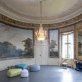 Gartensaal_Copyright_LVR-ZMB, Stefan Arendt 2024.jpg Eleganter, runder Saal mit historischen Wandmalereien, imposantem Kronleuchter und modernen Sitzhockern.