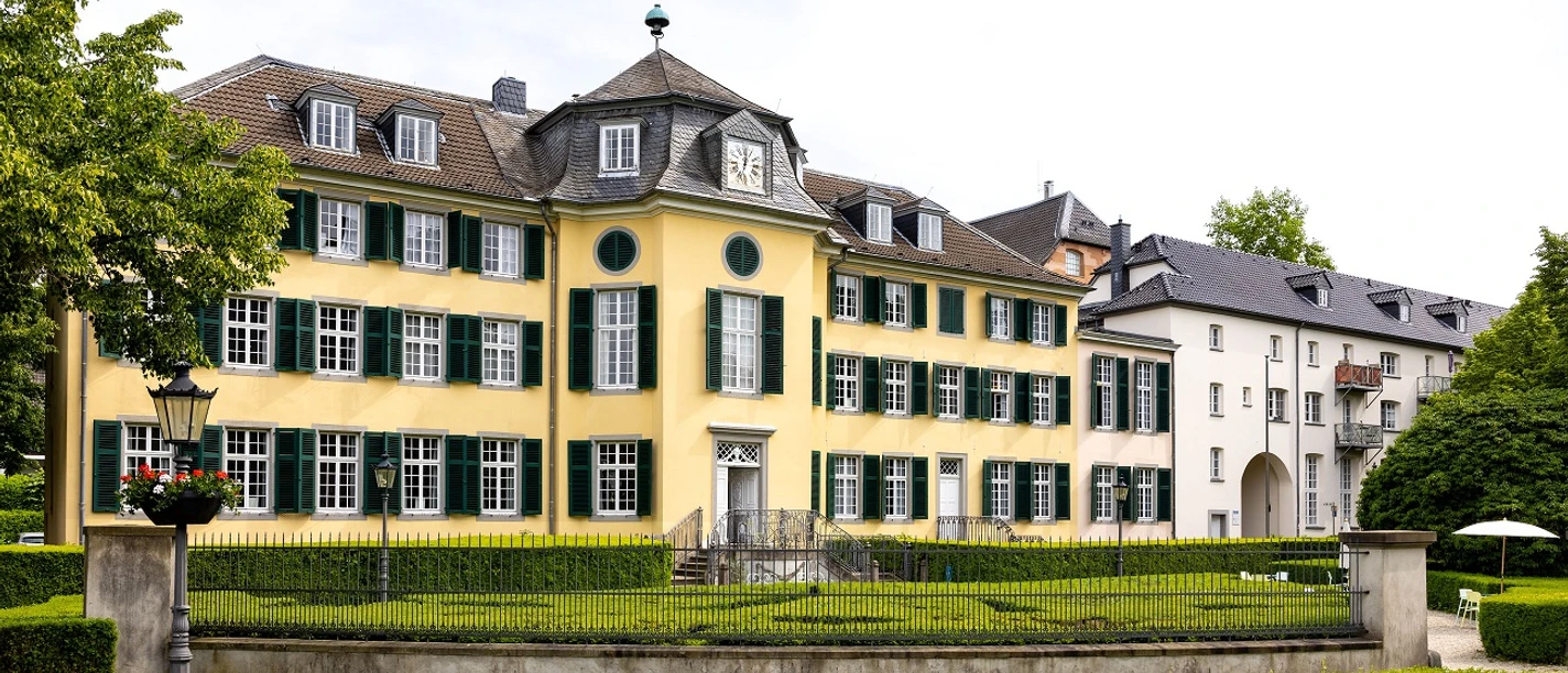 Herrenhaus Cromford Historisches Herrenhaus mit gelber Fassade, flankiert von grünen Fensterläden und gepflegter Gartenanlage.