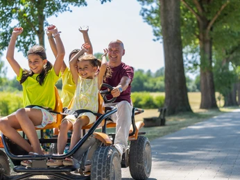 Gocart ausleihen im Monheimer Landschaftspark Familien genießen eine fröhliche Fahrt mit einem großen Gokart auf einem sonnigen Parkweg.